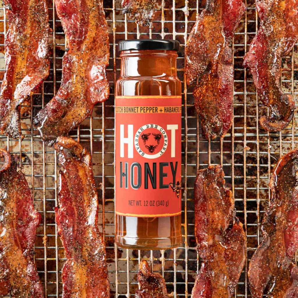 Hot Honey 12 oz. jar from Savannah Bee Company laying on the grill surrounded by bacon.