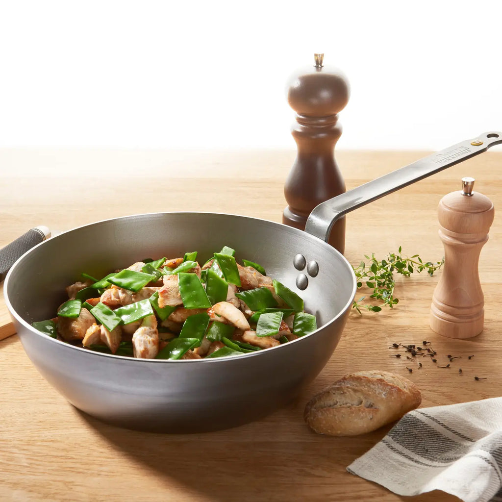 Wok with stir-fry on a wooden table with pepper grinder and bread