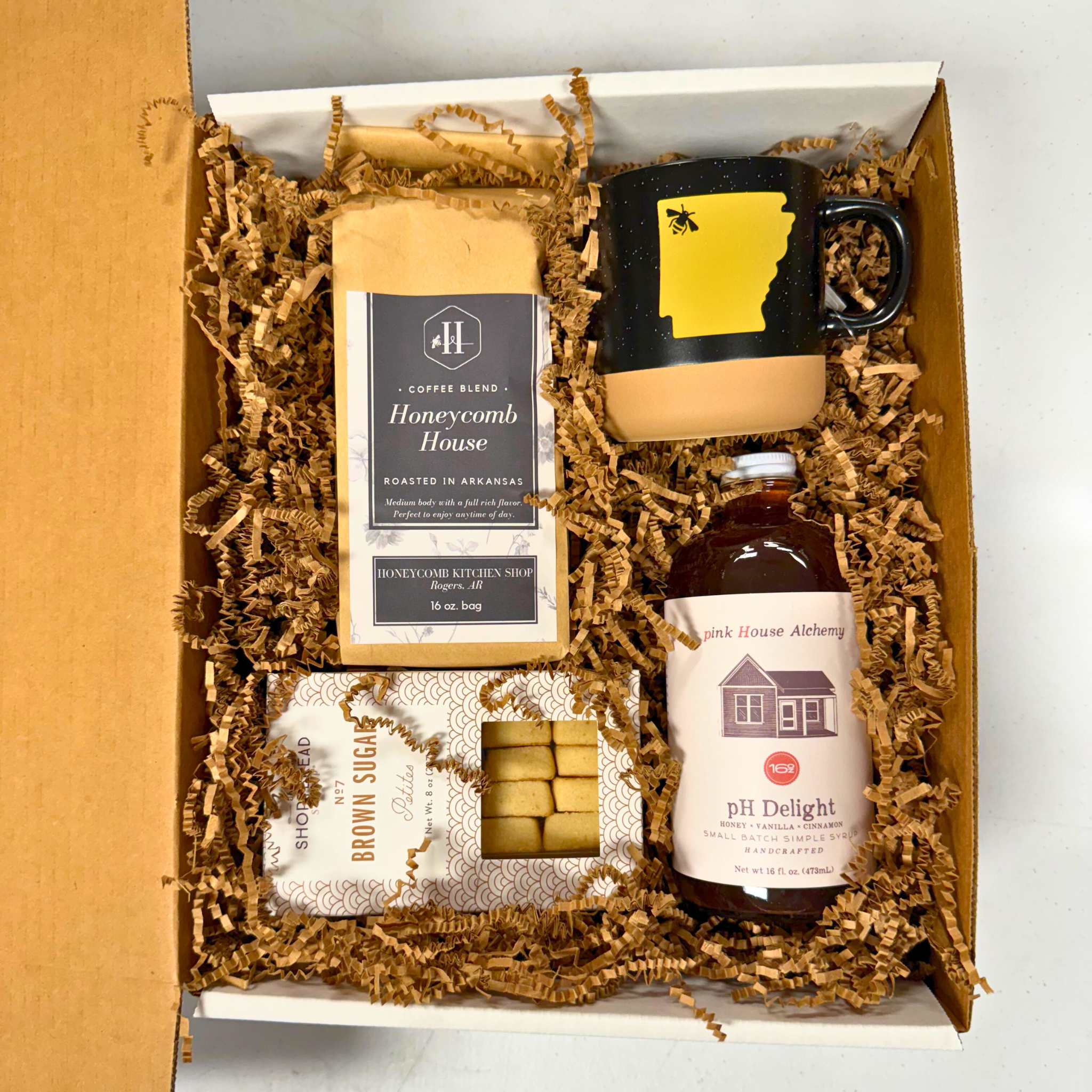 corporate gift includes 16 oz. coffee bag, ph delight simple syrup, shortbread cookies, and black mug with Arkansas shape in yellow with bee over NWA