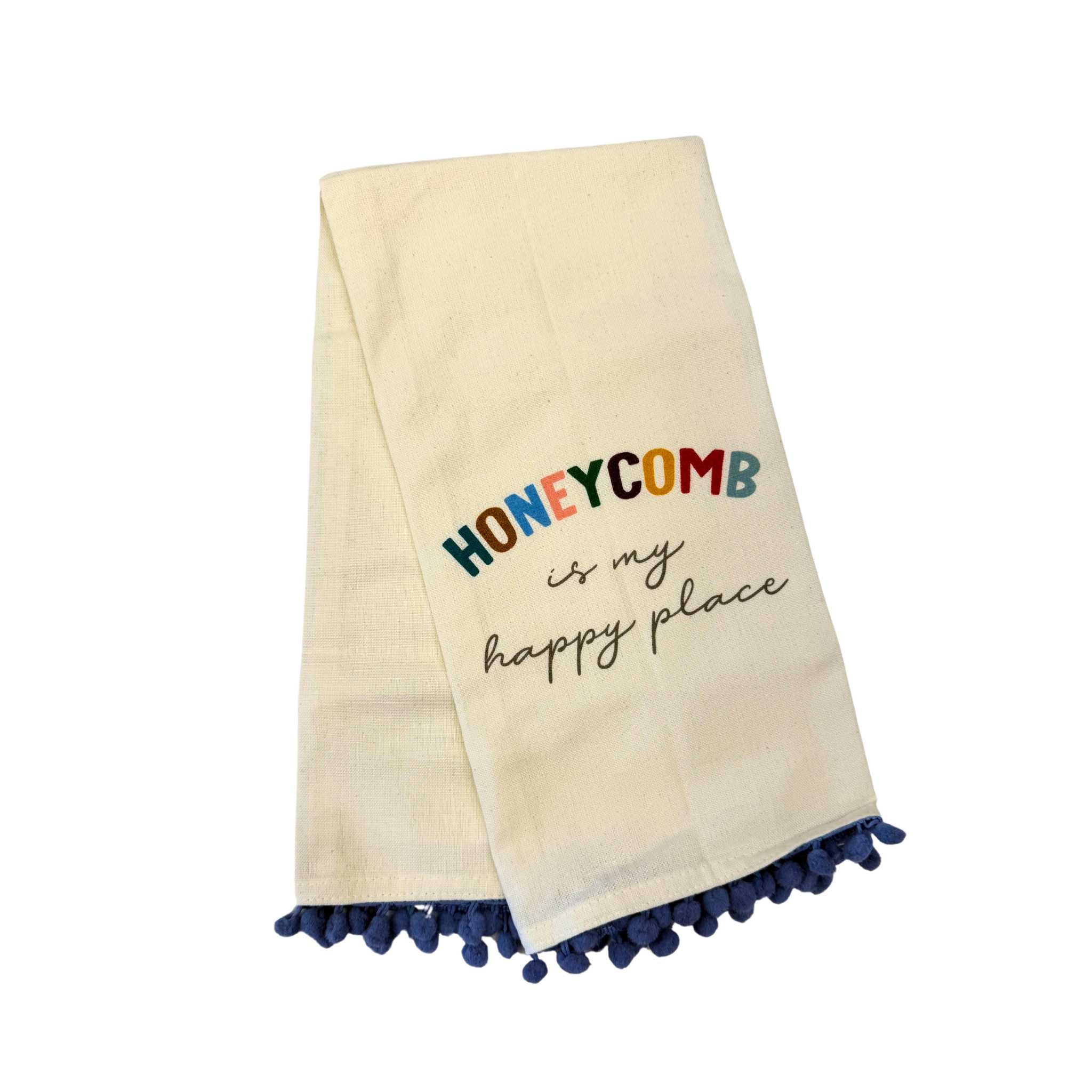 dishtowel that says honeycomb is my happy place. Dishtowel has blue small pom poms at the bottom.