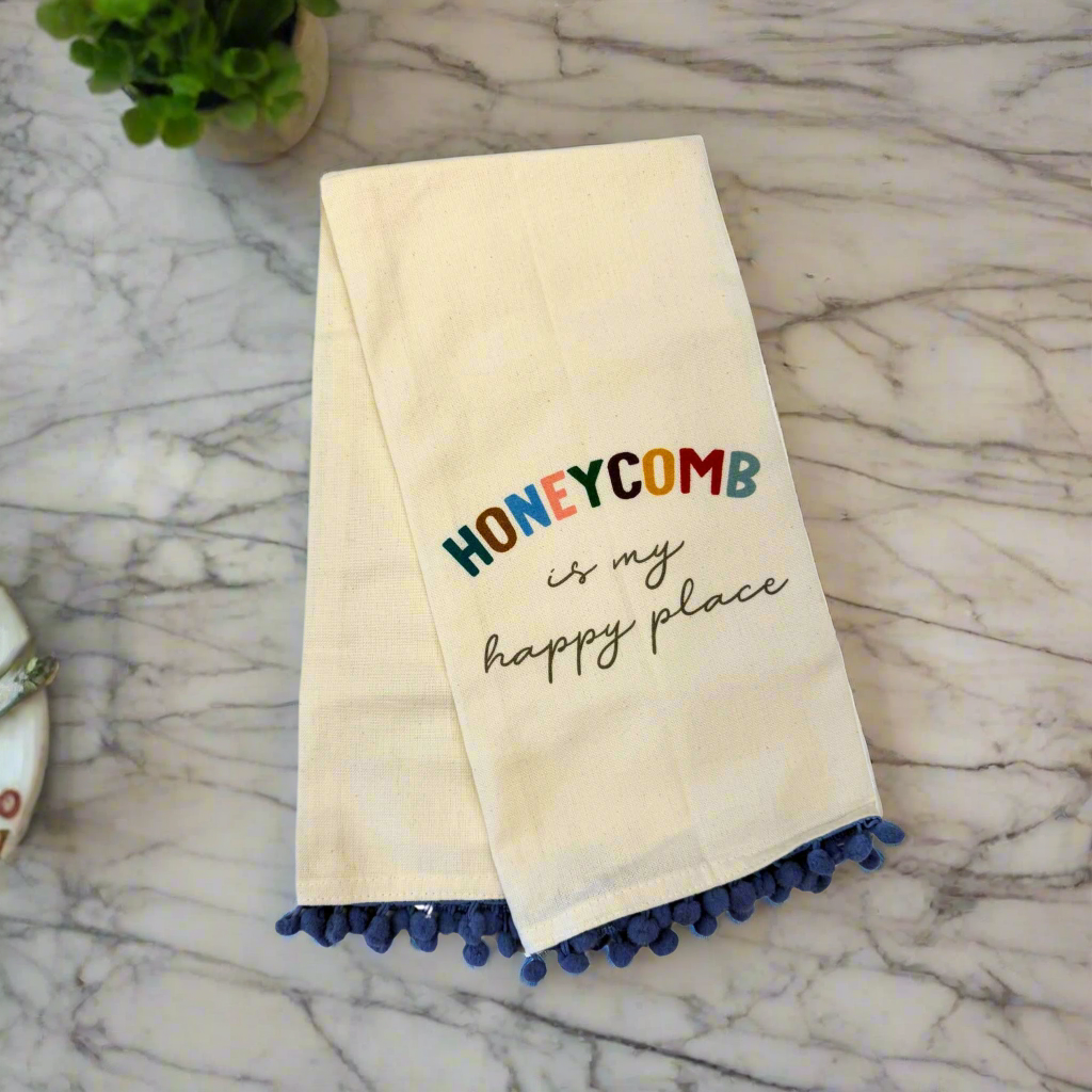 dishtowel that says honeycomb is my happy place. Dishtowel has blue small pom poms at the bottom.